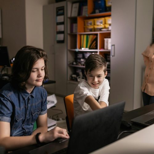 Students using laptops in a classroom setting with a teacher supervising, promoting digital education.